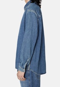 Camicia in denim azzurro chiaro, vestibilità rilassata, maniche lunghe con polsini abbottonati, dettagli di cucitura visibili, colletto alla cinese, orlo con spacchi laterali.