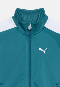 Τζελ αθλητικό μπουφάν με φερμουάρ, με ριμπ γιακά, λευκές πιέτες στους ώμους και λευκό λογότυπο Puma στο αριστερό μέρος του στήθους.