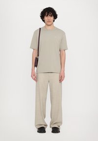 Lichtgrijze korte mouwen t-shirt gecombineerd met beige, loszittende broeken en zwarte schoenen, met een kleine bruine schoudertas.