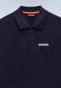Mørkeblå polo-skjorte med teksturert stoff. Har en tre-knapps placket, en oransje detalj inne i kragen og en hvit logo.
