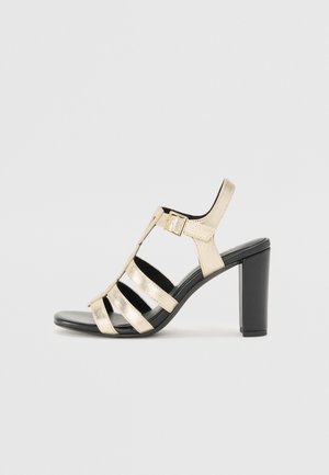 Gold metallic heeled sandal with multiple black straps and a side buckle. The heel is solid black and the sole is smooth and flat.