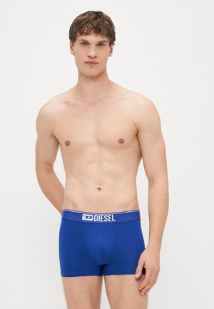 Boxeri din bumbac albaștri cu o talie elastică decorată cu un logo alb. Textură netedă și design ajustat. Modelul este fără cămașă.