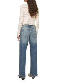 Hoch-taillierte, weit geschnittene Jeans aus hellblauem Denim mit fünf Taschen und fransigen Saumdetails. Kombiniert mit einem langärmligen gestreiften Oberteil.
