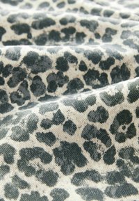 Leopard print fabric featuring a textured surface with dark green spots on a light cream background, draped in soft folds.