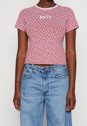 Person trägt ein rotes, bauchfreies T-Shirt mit weißem Blumenmuster und weißem "Levi's"-Logo, kombiniert mit hoch taillierten hellblauen Jeans.