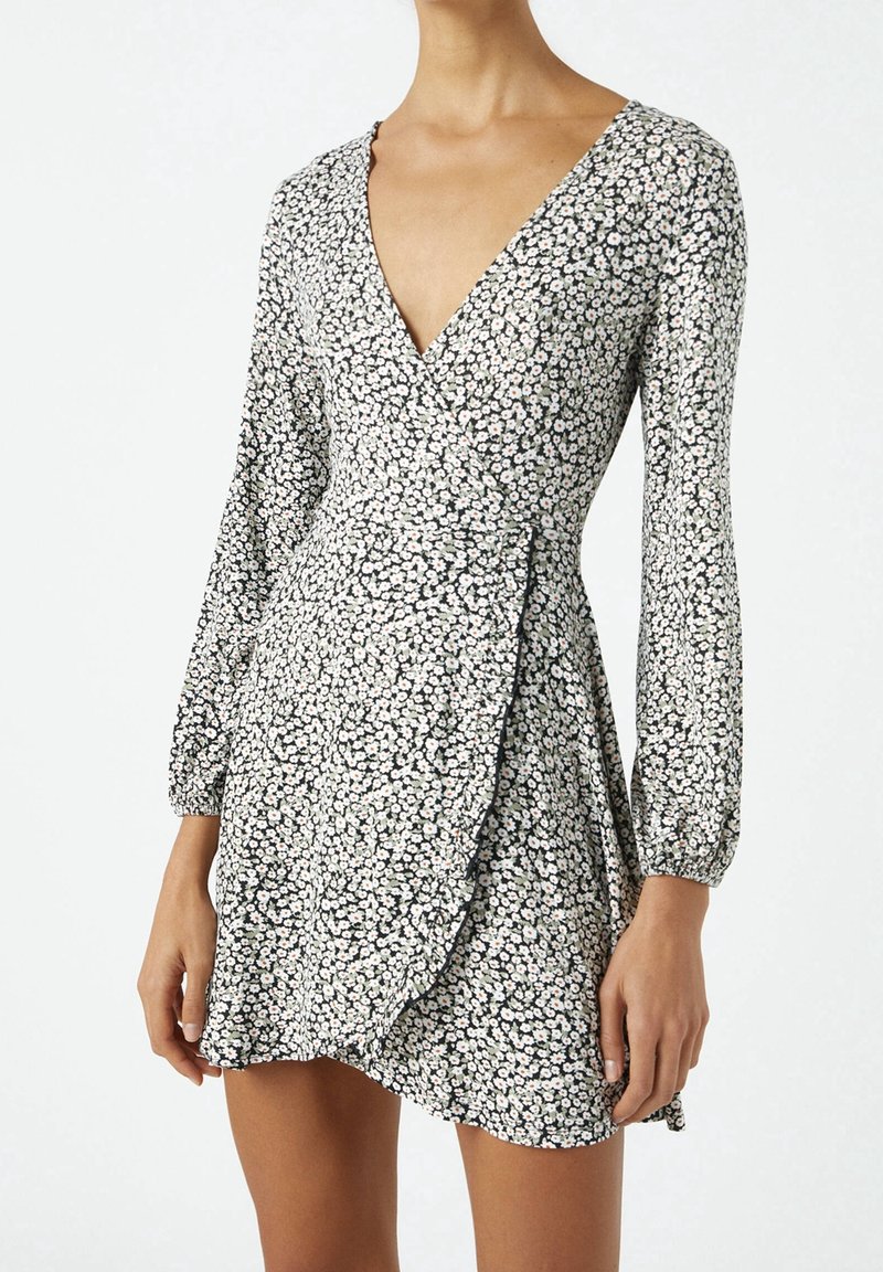 Vestido envolvente floral con mangas largas, con un escote en V profundo, fondo negro, pequeñas flores blancas y un dobladillo con volantes.
