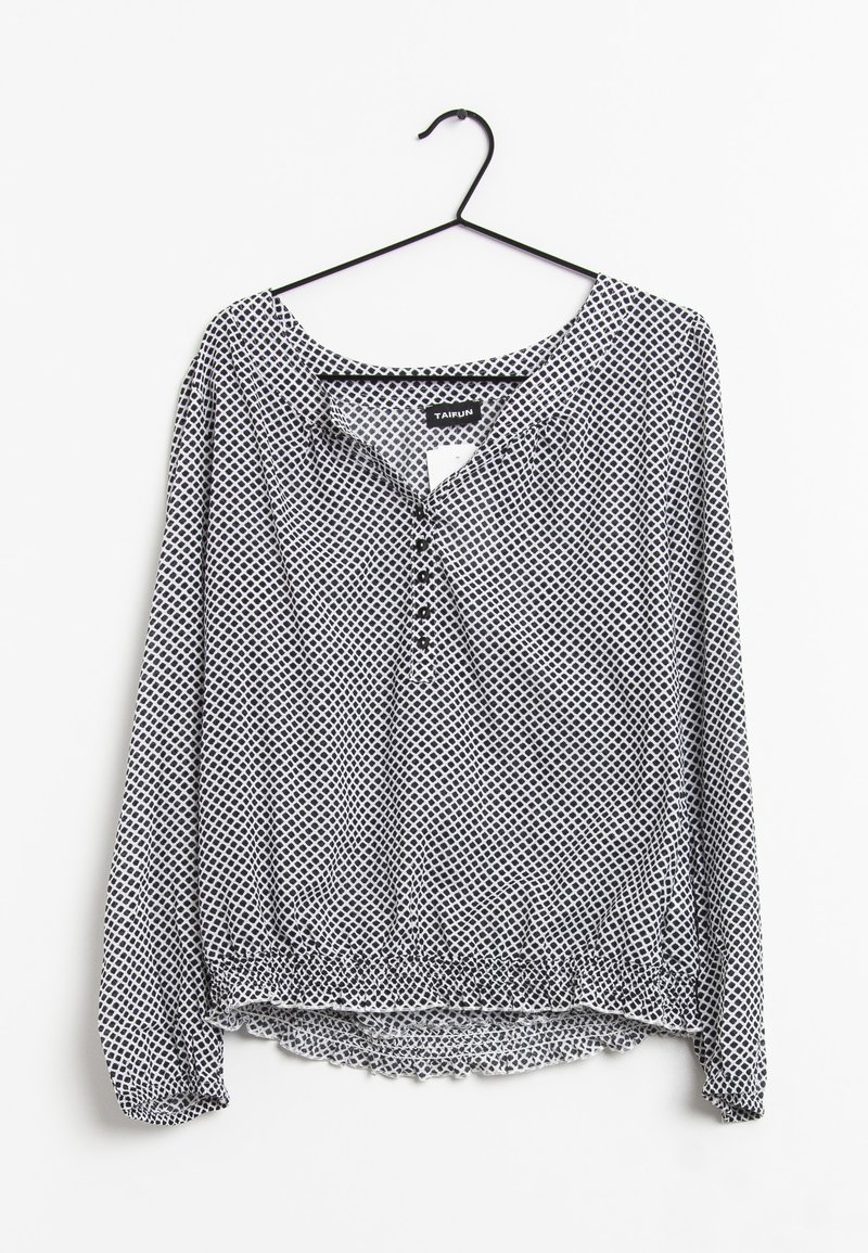 Blusa a maniche lunghe con motivo bianco e nero, orlo elastico e scollatura con bottoni, appesa a una gruccia nera su sfondo bianco.