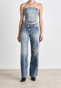 Top corto in denim con arricciatura sul petto; jeans blu a vita alta con lavaggio sbiadito e gamba dritta; stivali neri alla caviglia.