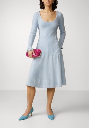 Lichtblauwe geribbelde gebreide jurk met een ronde halslijn, aangesloten lijfje, uitlopende rok en lange mouwen, gecombineerd met een roze pailletten clutch en blauwe hakken.