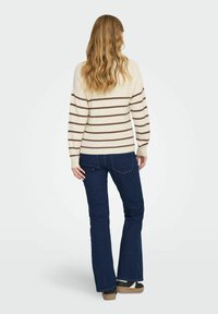 Suéter crema con rayas marrones horizontales, mangas largas y un corte relajado. Combinado con jeans acampanados de color azul oscuro y zapatos de plataforma.