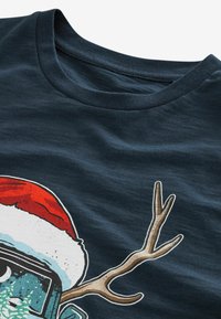 Mørkeblå bomulds T-shirt med rund hals, med et grafisk motiv af en julesok og gevir i livlige røde, hvide og brune nuancer.