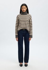 Csíkos garbó pulóver bézs és szürke színekben, sötétkék egyenes szárú farmerrel és fekete balerinacipővel párosítva, kényelmes szabással és bordázott mandzsettákkal.