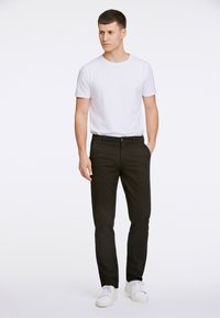 Pantaloni neri in cotone con design a gamba dritta, abbinati a una t-shirt bianca aderente e sneakers bianche. Abbigliamento semplice e casual.