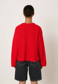 Pull rouge côtelé avec une coupe décontractée, des manches larges et une longueur cropped, associé à un short noir délavé avec des bords effilochés.