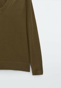 Pull en maille vert olive avec manches longues, encolure en V et ourlet côtelé. Texture douce et coupe ajustée avec des détails minimalistes.