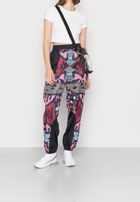Colorful, patterned track pants with pink, black, and gray hues; elastic waistband; paired with a white cropped t-shirt and sneakers.