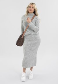 Maglione grigio a coste e gonna abbinata, abbinati a una piccola borsa marrone e sneakers platform bianche, su uno sfondo neutro.