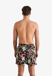 Bloemige zwemshorts met een zwarte achtergrond, voorzien van levendige roze, witte en groene botanische patronen. Elastische tailleband met een achterzak.