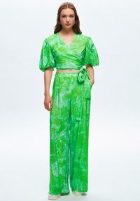 Groene, gestructureerde wrap-top met pofmouwen en bijpassende high-waisted wijde pijpen, voorzien van een gestrikt detail en subtiele patronen.