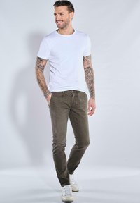 White short-sleeve t-shirt, olive green slim-fit pants, and white sneakers, with visible tattoos on arms. Simple design, casual style.