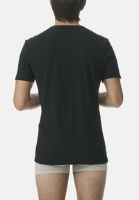 Camiseta negra de manga corta hecha de algodón suave, con cuello redondo y un ajuste holgado, vista desde la parte de atrás con una textura suave.