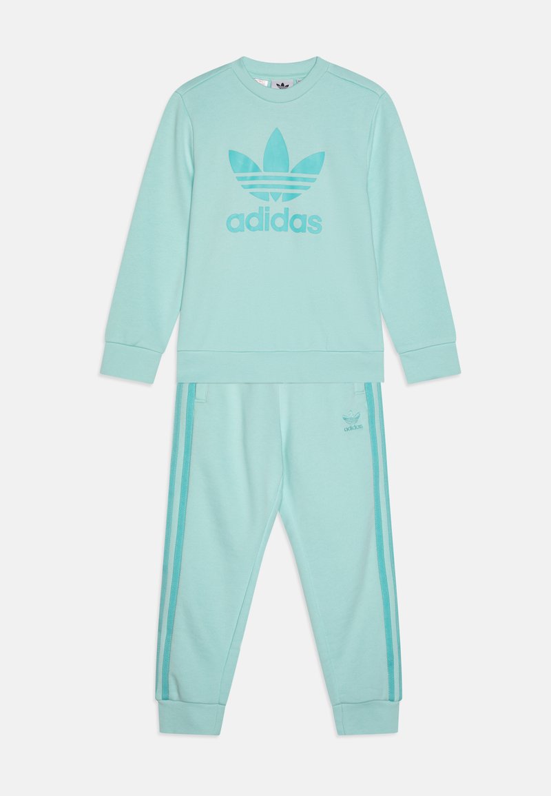 Mėtų žalios spalvos adidas džemperis ir kelnių komplektas. Džemperis turi didelį logotipą, minkštas rankogalius ir atitinkamas šonines juosteles ant kelnių.