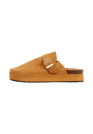 Tanhvid læder-slip-on-træsko med gyldne nitter, justerbar spænde-rem og tyk platformsål med mørkædt bund.