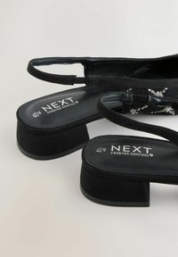 Sorte suede sandaler med blokhæl og tynde stropper. Egenskaber inkluderer et struktureret overmateriale og polstrede indersåler for komfort. Mærkeetiketten er synlig.