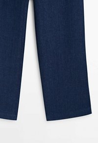 Jambes de pantalon en jean bleu foncé avec ourlets droits affichées sur fond blanc.