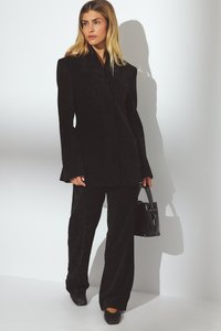 Completo in velluto nero caratterizzato da un blazer su misura con spalle strutturate e pantaloni a gamba larga. Accentuato con una piccola borsa nera e scarpe a punta.