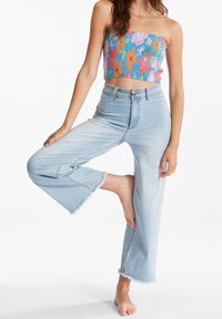 Top corto sin tirantes con un patrón floral multicolor; combinado con jeans de pierna ancha de color azul claro, con dobladillo deshilachado y cintura alta.