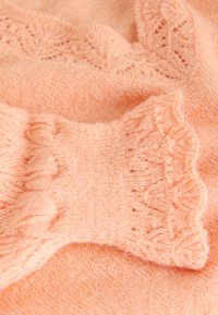 Brzoskwiniowy sweter dziany z prążkowanym wzorem i delikatnymi łuskowatymi mankietami. Miękka faktura z koronkowym wzorem przy dekolcie.
