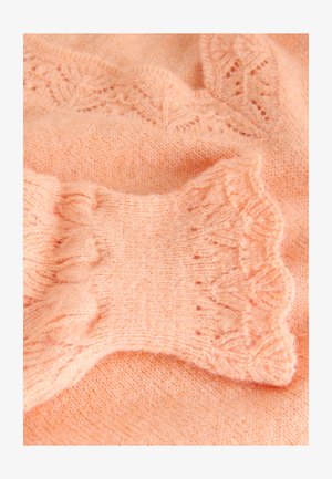 Pfirsichfarbener Strickpullover mit Rippendesign und zarten, gewellten Bündchen. Weiche Textur mit einem Spitzenmuster entlang des Halsausschnitts.