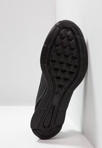 Semelle de chaussure de sport noire avec une surface en caoutchouc texturé présentant un motif géométrique, idéale pour l'adhérence et la traction.