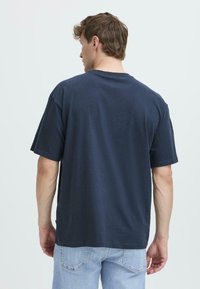 Camiseta oversized en algodón de color azul marino oscuro, con mangas cortas, cuello redondo y una textura suave, combinada con pantalones vaqueros de mezclilla azul claro.