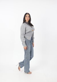 Cardigan grigio in maglia con maniche a sbuffo, dotato di chiusura con bottone in legno. Abbinato a jeans dritti in lavaggio chiaro e sandali con tacco trasparente.