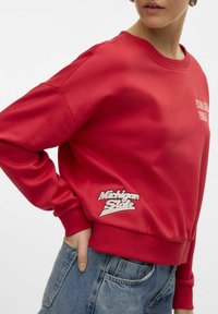Sweatshirt rouge avec un col rond, présente le texte "Établi en 1960" et "Michigan State" brodé en blanc sur le bas à l'avant.