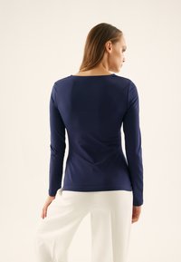 Navy long-sleeve top with a rounded neckline and fitted design. Made of smooth fabric, paired with white wide-leg trousers.
