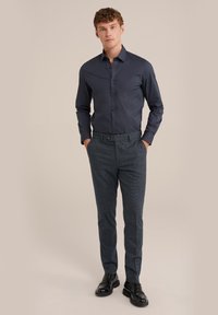 Chemise bleu marine à boutons et manches longues, associée à un pantalon gris à motifs. Des chaussures noires impeccables complètent le look.