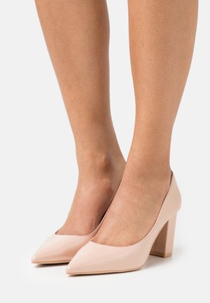 Escarpins en cuir verni nude à talons hauts, avec une pointe pointue et un talon bloc, présentant une texture lisse et brillante ainsi que des détails de couture minimalistes.