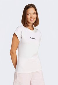 Balti apvalių kaklo marškinėliai trumpomis rankovėmis, ant krūtinės yra juodas „Adidas“ logotipas, pagaminti iš lygaus, lengvo audinio.