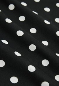 Fekete anyag, egyenletesen elrendezett fehér pöttyökkel, enyhe hajtásokkal és textúrával.
