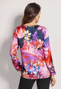 Bunte Blumenbluse mit langen Ärmeln, rundem Ausschnitt und glänzender Satinoptik. Die Hauptfarben sind Pink, Blau und Rot.