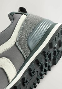 Gray sneaker with textured suede and fabric upper, featuring a white accent stripe, a ribbed gray heel, and a patterned black rubber sole.