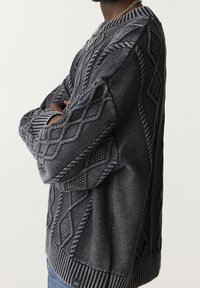 Pull gris tricoté avec un design texturé comprenant des motifs en losange et en torsades. Poignets et ourlet côtelés, coupe décontractée.