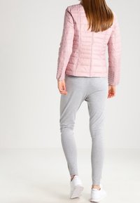 Hellrosa gesteppte Jacke mit taillierter Passform, kombiniert mit grauen Jogginghosen. Das Outfit hat eine glatte Textur und einen lässigen Look, abgerundet mit weißen Sneakern.