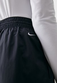 Čierne športové šortky s elastickým pásom a bielym logom Nike na ľavej strane, spárované so svetlošedým dlhým rukávom.