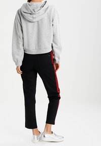 Persona che indossa un hoodie grigio e pantaloni neri con righe rosse, in piedi, con ai piedi delle scarpe slip-on argentate.