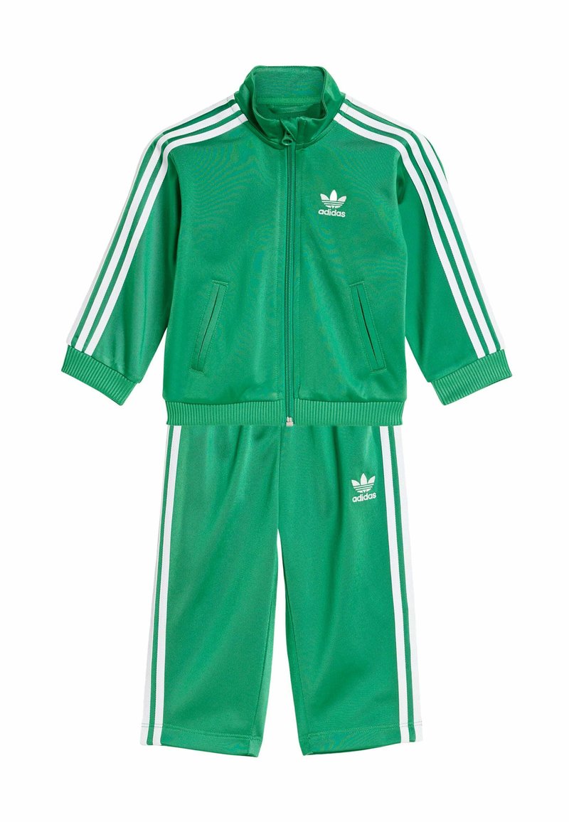 Zielony dres Adidas wykonany z gładkiego poliestru; bluza na zamek z białymi paskami i logo; pasujące spodnie z elastycznym paskiem w talii, o długości 7/8.
