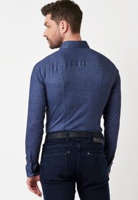 Donkerblauwe overhemden met gestructureerde kraag en lange mouwen, gemaakt van een textuurstof en een getailleerde pasvorm, gecombineerd met donkerblauwe jeans.